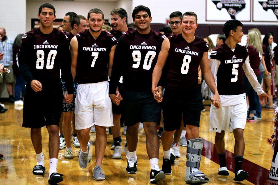 Football Captains hold hands as they lead the procession of football players through the gym, marking the start of the pep rally. Holding hands is a tradition they take part in at the beginning of each game. 