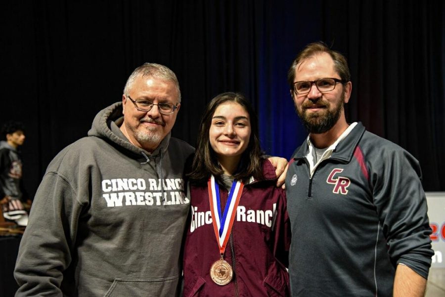 Coaches Bill Dushane and Luke McConn stand with junior Isabella Walsh after she receives her fourth place medal.
