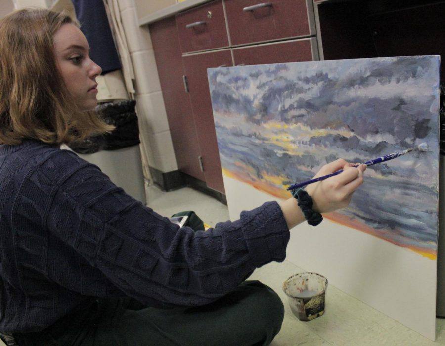 A National Art Honor Society student works on a painting of a sunset.